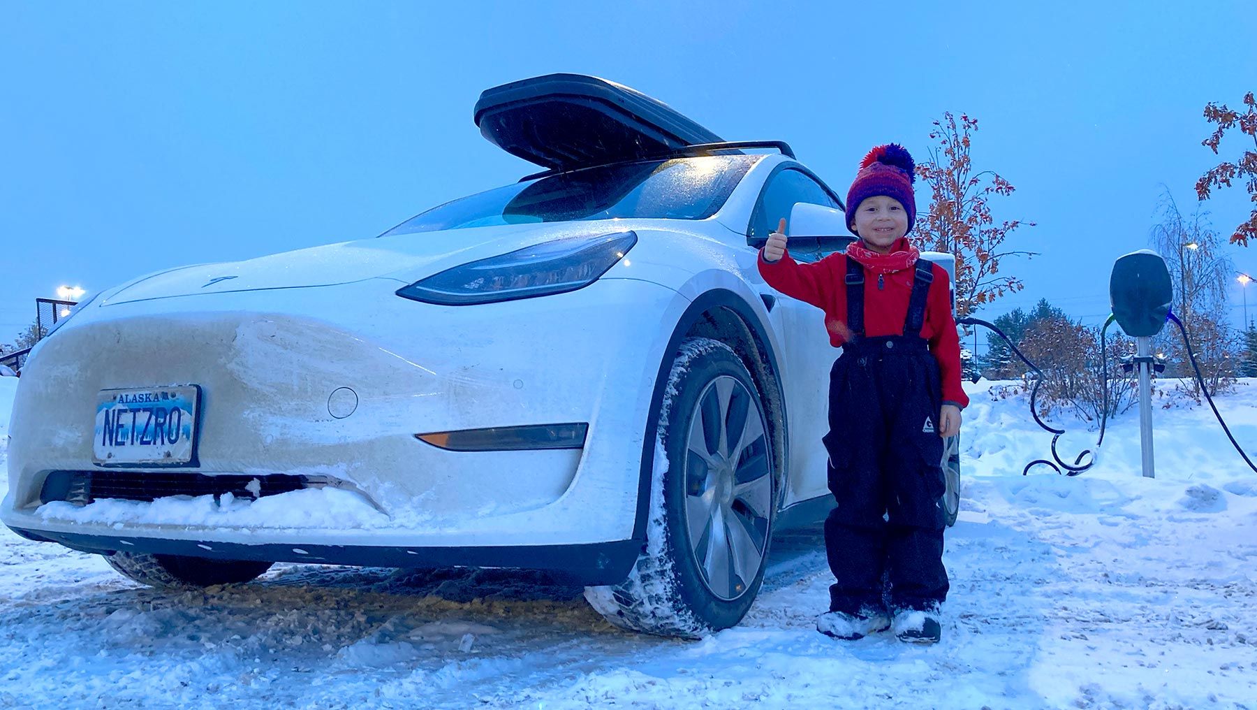 Kid giving thumbs up, standing by electric car